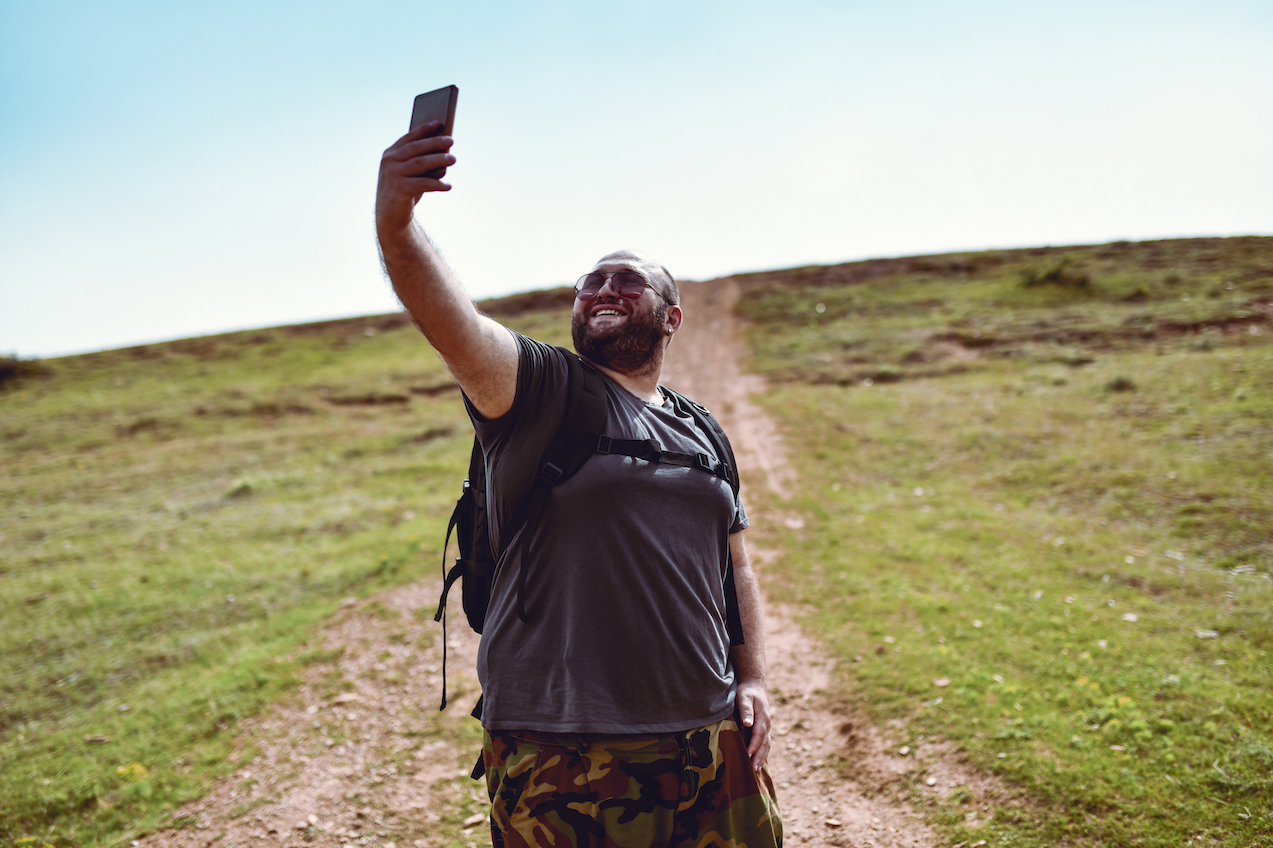 Male hiker taking selfie with smartphone while walking uphill