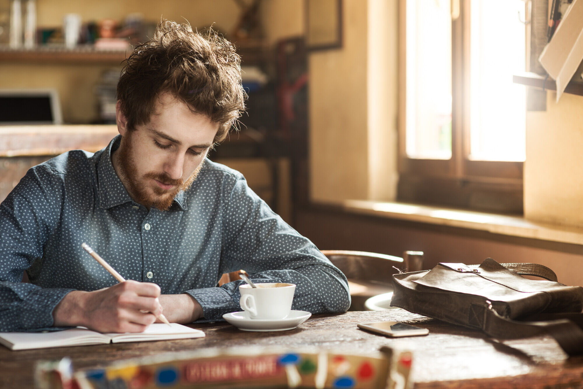 Young hipster man sketching on a notebook in his studio on a rustic wooden table