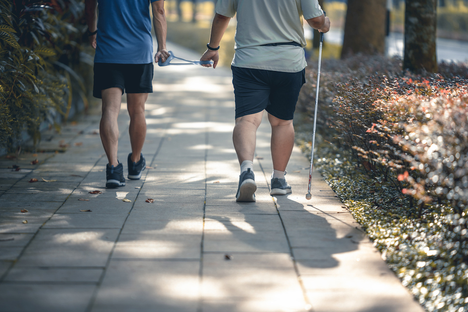 Asian Chinese visually impaired mature man holding running tether in public park with guide runner